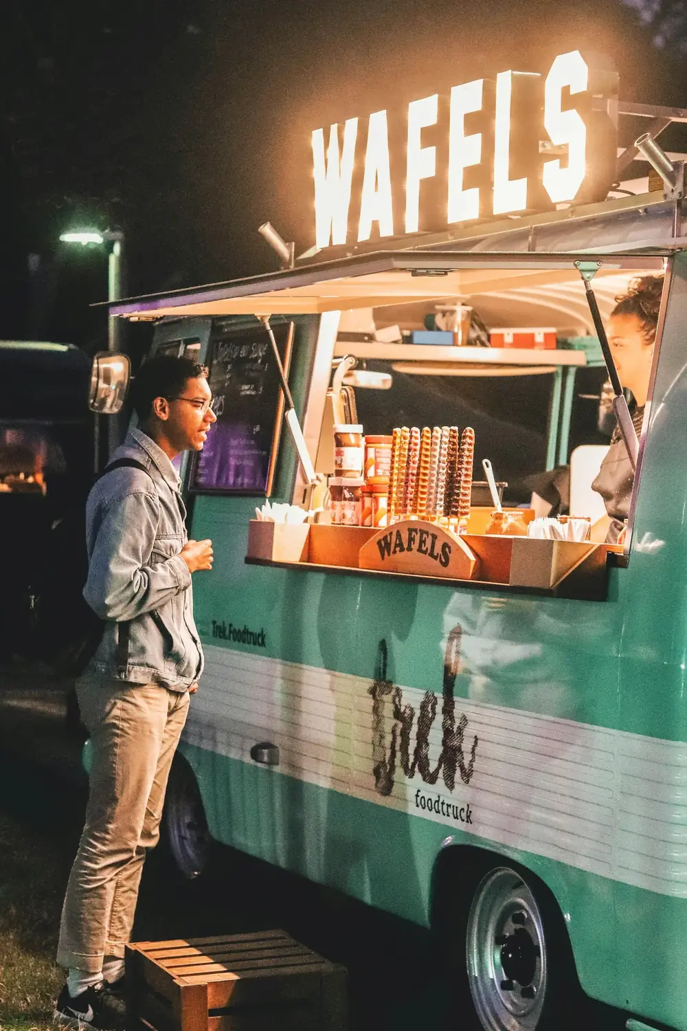 A customer being served at a lit food truck at night